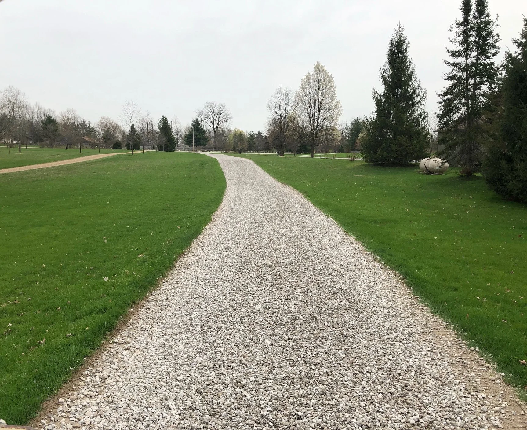 A freshly installed gravel driveway at a residential property in Charlotte, NC, with evenly spread stone, clean edges, and a graded surface sloping away from the home. B&D Construction driveway gravel work on a single-family lot with red clay soil visible at the driveway border.