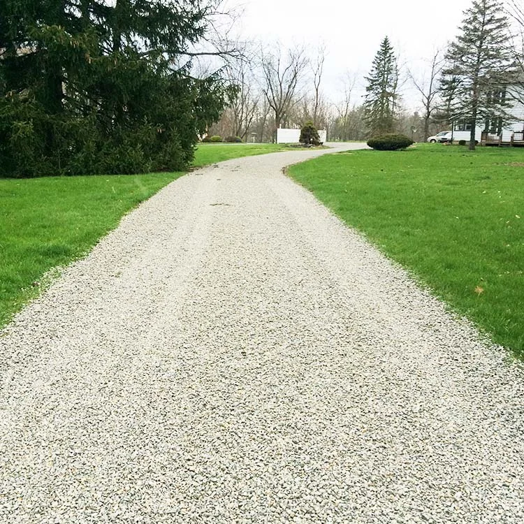 A freshly installed crushed limestone driveway at a Charlotte, NC residential property, showing a compacted light gray stone surface leading to a two-car garage. The natural stone color contrasts with the surrounding green lawn and brick home exterior.